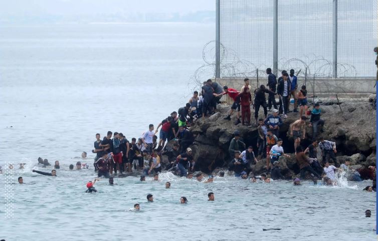 مواطنون مغاربة يقفون بجوار السياج الفاصل بين الحدود الإسبانية المغربية ويسبحون حوله في مايو/أيار الماضي (وكالات) 