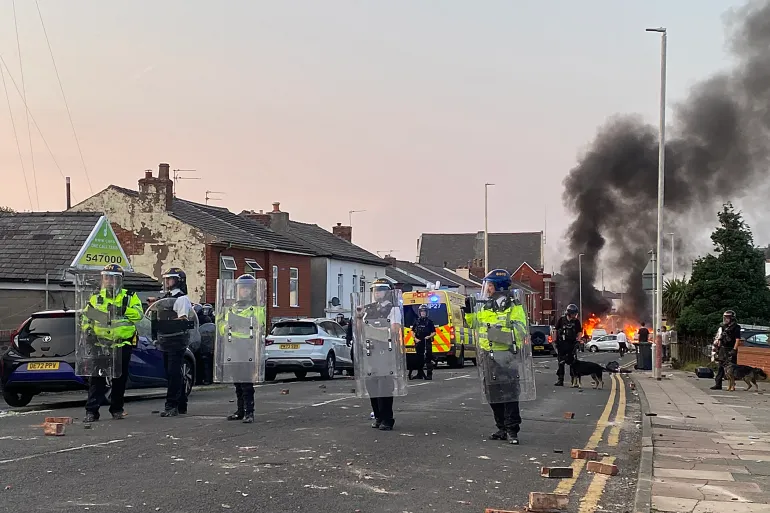 Protesters set a fire as riot police stand guard near the Southport Islamic Society Mosque [Lloyd Parry/AFP]