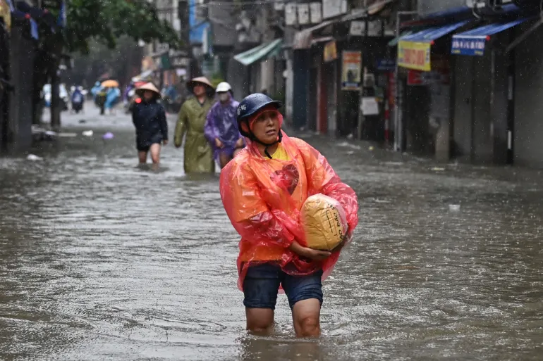 A woman carries a bag of rice in Hanoi, on September 11, 2024, as heavy rains in the aftermath of Typhoon Yagi brought flooding to northern Vietnam, with river levels hitting a 20-year high and the death toll reaching at least 179 [Nhac Nguyen/AFP]