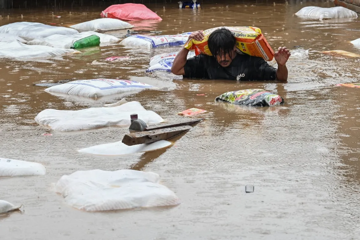 A man carrying a sack of flour wades through floodwaters after the Bagmati River overflowed following heavy monsoon rains in Kathmandu. [Prakash Mathema/AFP]