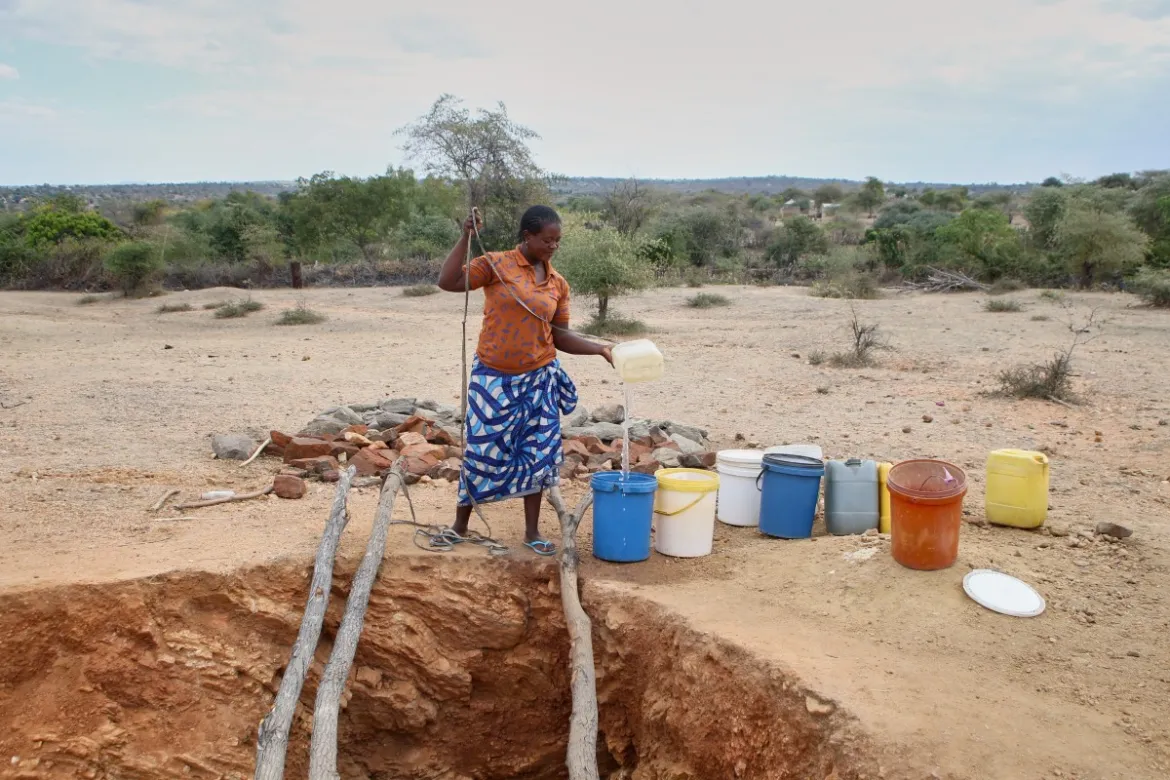 A woman in Mudzi draws water at a village well, which has very limited reserves of water remaining. [Jekesai Njikizana/AFP]