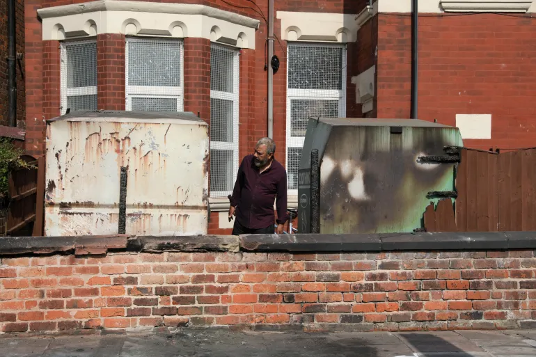 A man inspects damaged clothing bins and a fence of the Southport Mosque on July 31, 2024, after a violent protest following a vigil for victims of the knife attack in Southport, Britain [Temilade Adelaja/Reuters]