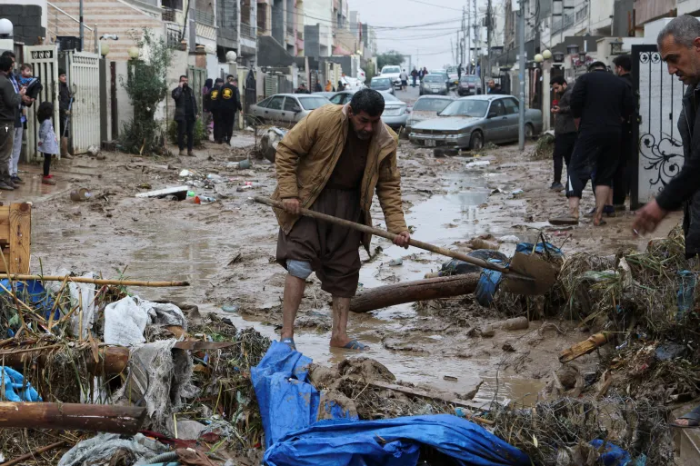 Residents clean a road full of mud after flash floods caused by torrential rains in Erbil [Azad Lashkari/Reuters]