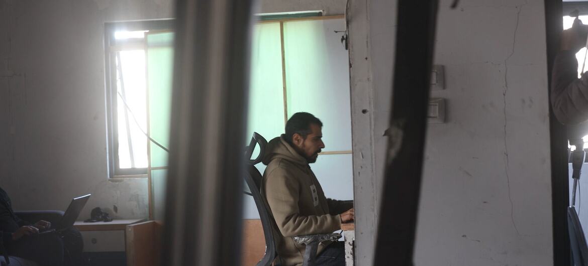 UN News A journalist works in the damaged office of Zaman 90.60 FM radio station in Gaza City.