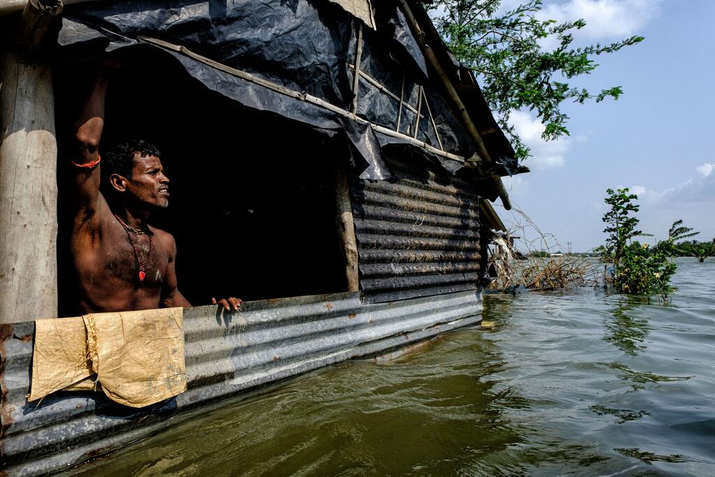 © Ocean Image Bank/Dipayan Bose A man stands in the doorway of his flooded tin-roofed home in a coastal village in India.